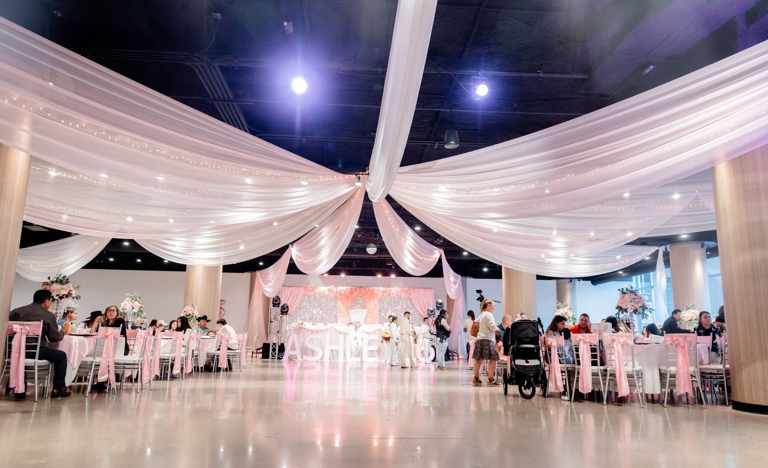 Elegant white wedding reception venue with draped fabric ceiling and circular table arrangements.