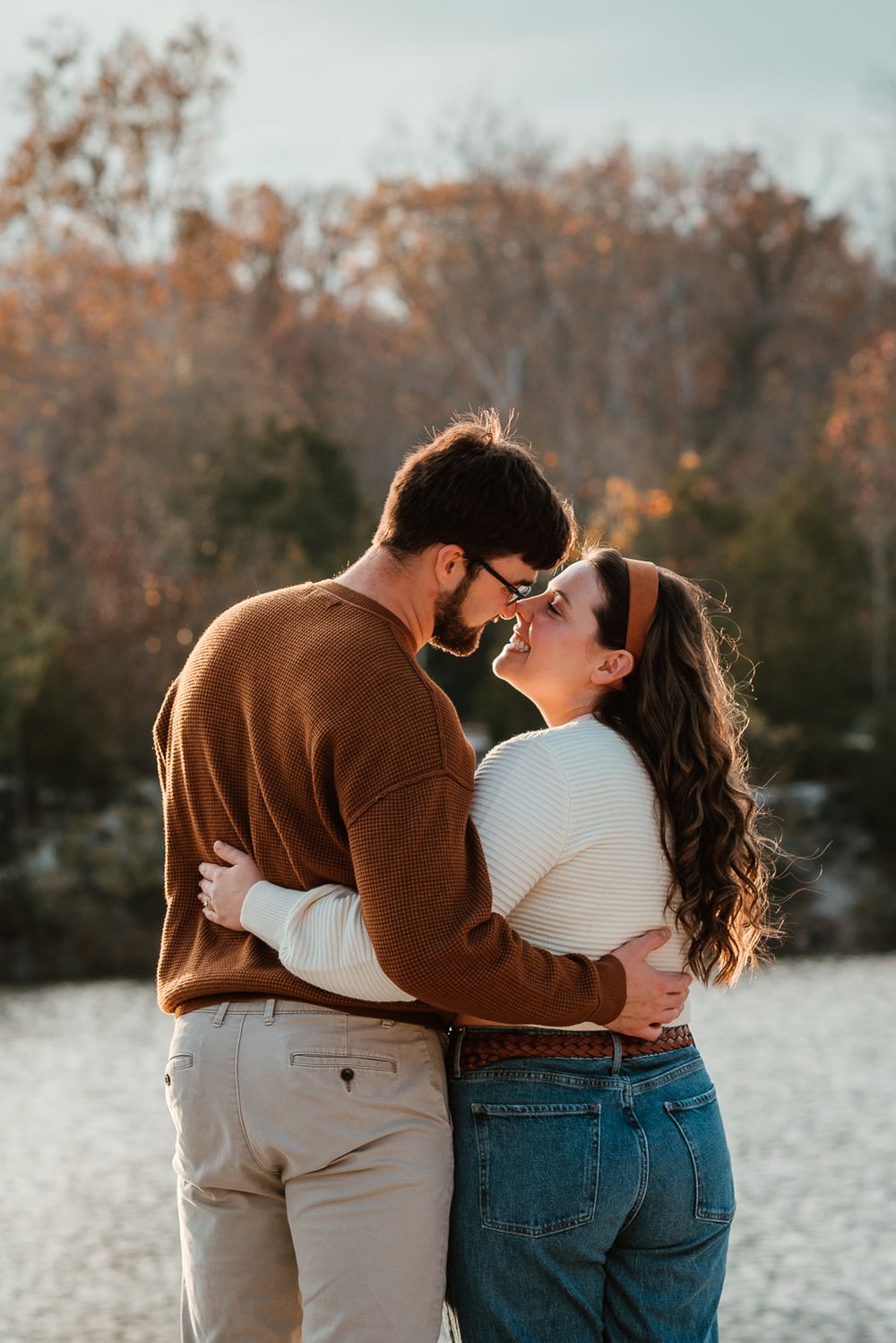A couple in casual attire sharing an intimate moment against a winter lakeside backdrop.