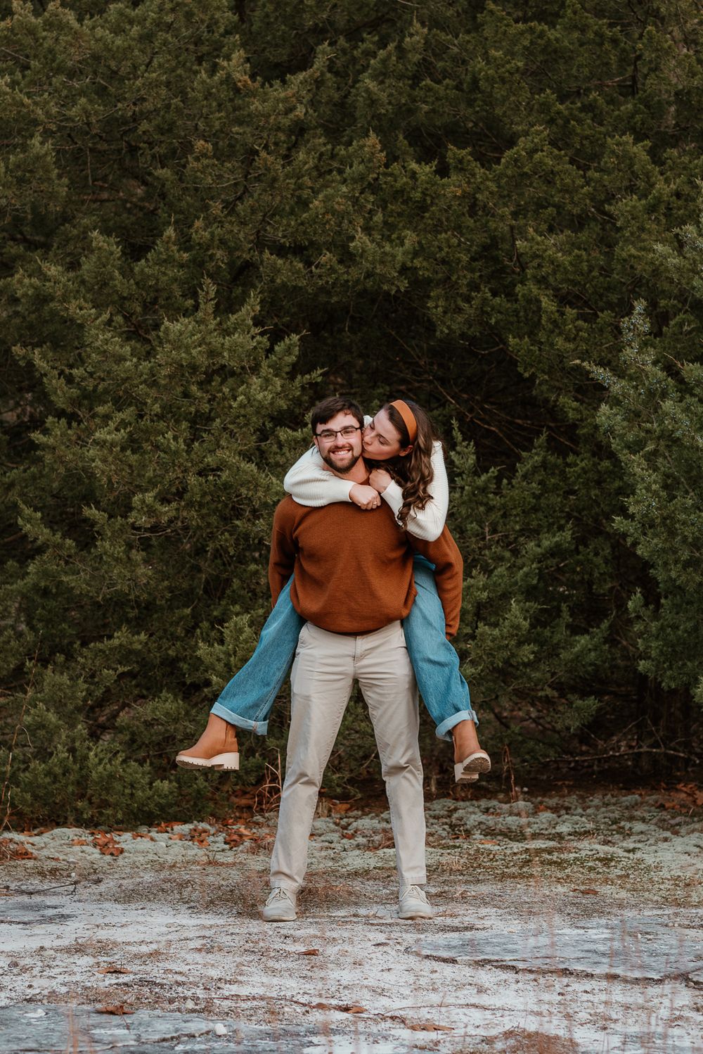 A playful couple posing together on rocky terrain surrounded by evergreen trees.