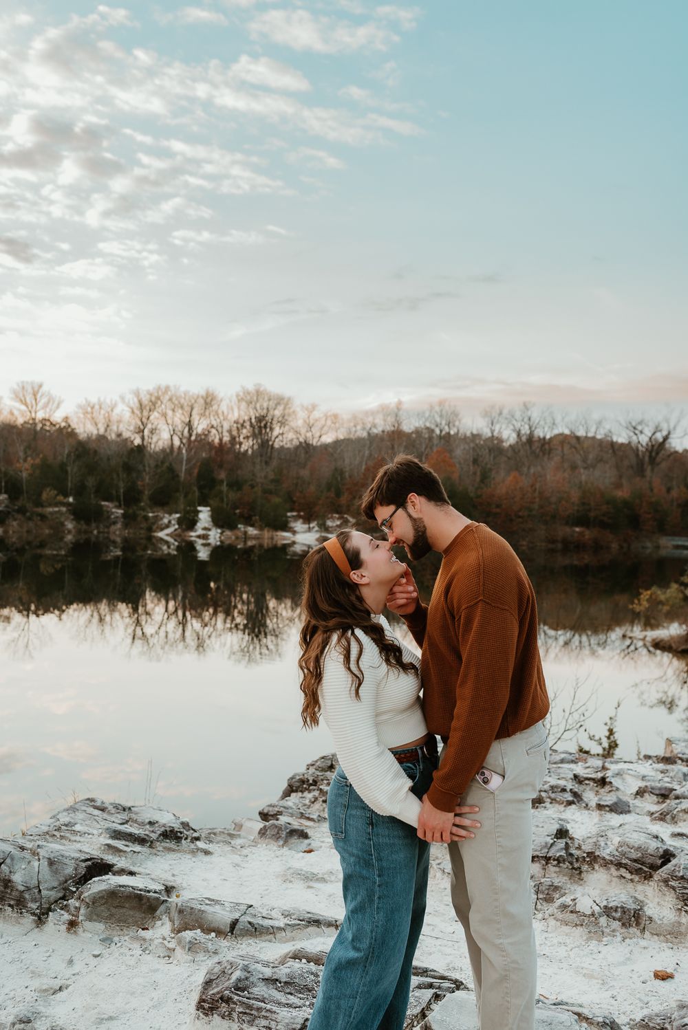 A romantic couple embracing by a serene lake during golden hour.
