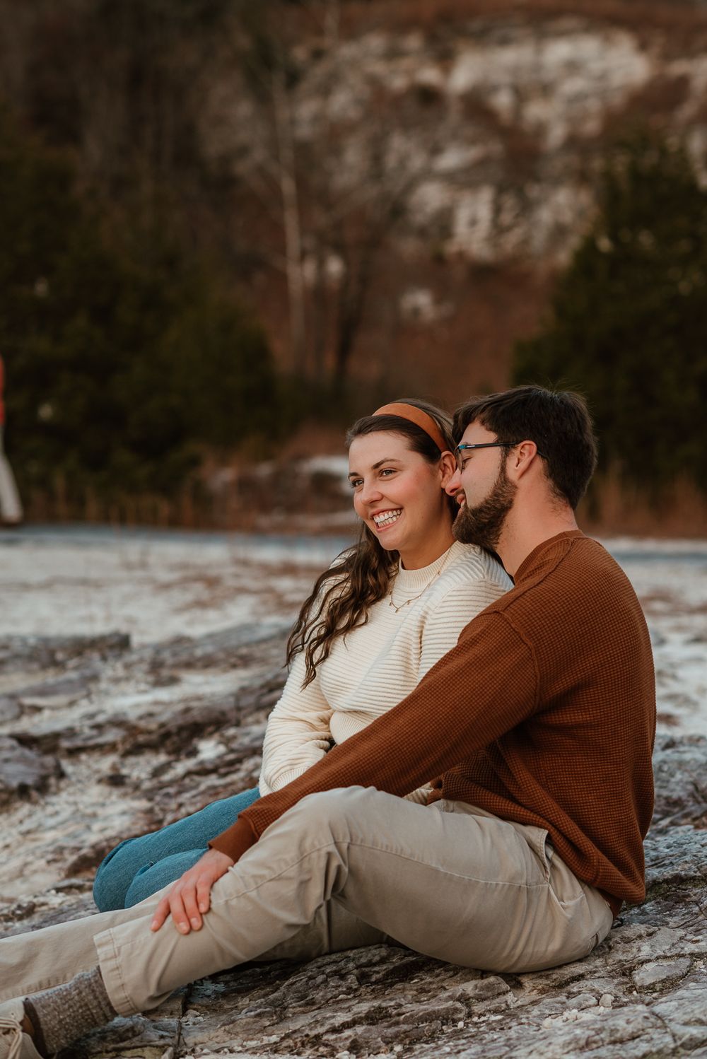 A couple sharing a tender moment while sitting on rocky ground during sunset.