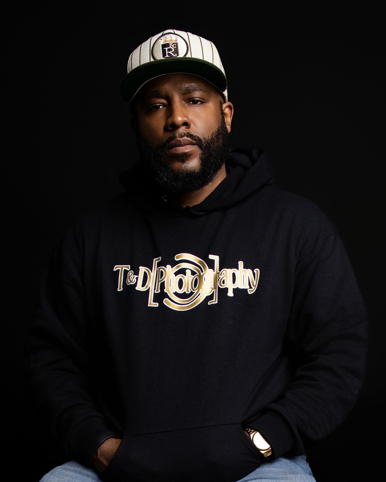 Black and white portrait of a bearded man wearing a wide brim hat and T&D Photography branded t-shirt.