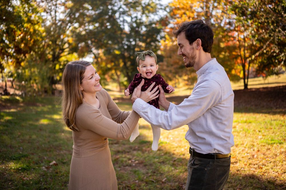 A playful family moment captured in a park with beautiful fall colors in the background.