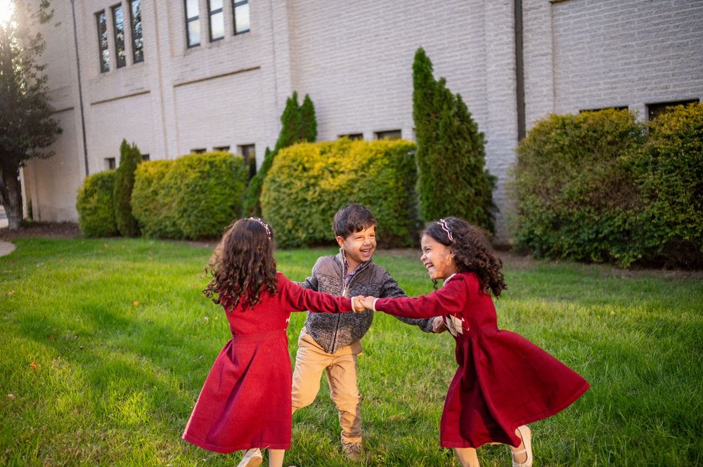 Four sequential images capture people interacting playfully on a grassy lawn beside a building in red outfits.