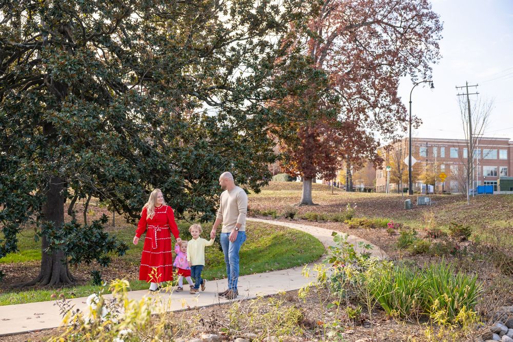 People walk along a winding garden path through autumn foliage and flowering plants in an urban park setting.
