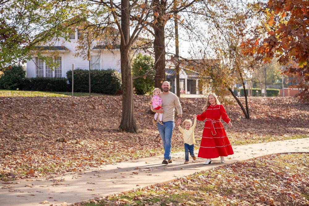 A scenic autumn path through a park with fallen leaves and people walking along a winding trail.