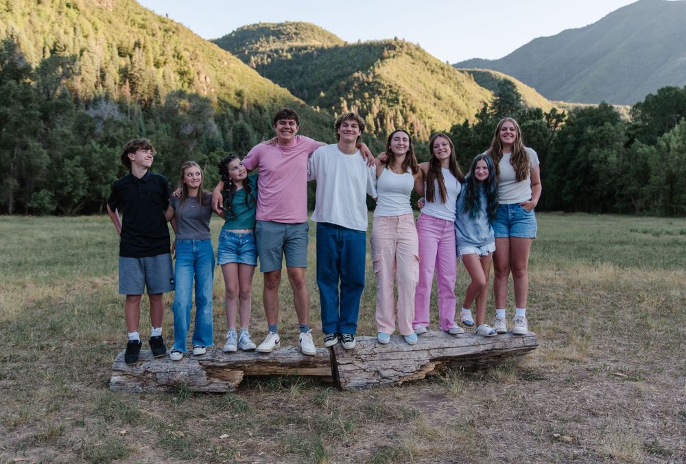 Group photo of friends standing together on wooden platform with mountain landscape behind.