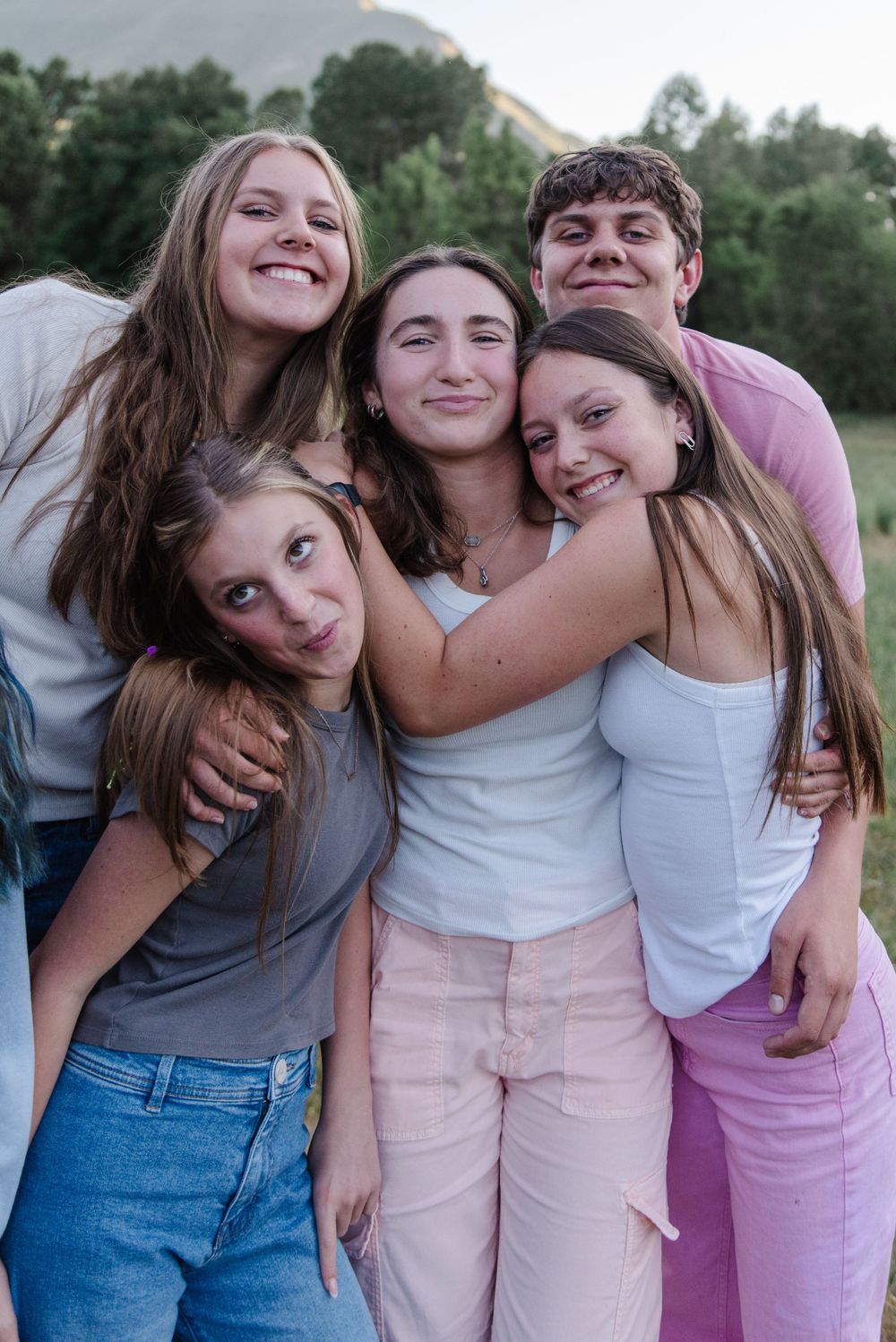 Group of friends hugging and smiling together outdoors in casual summer attire.