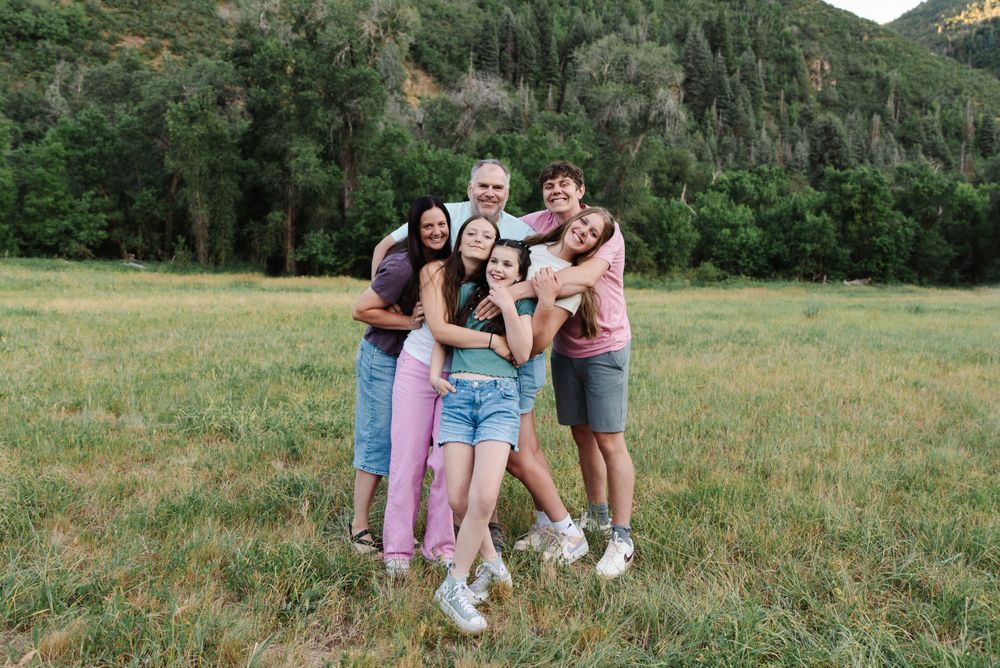 Group of friends embracing and laughing together in mountain meadow.