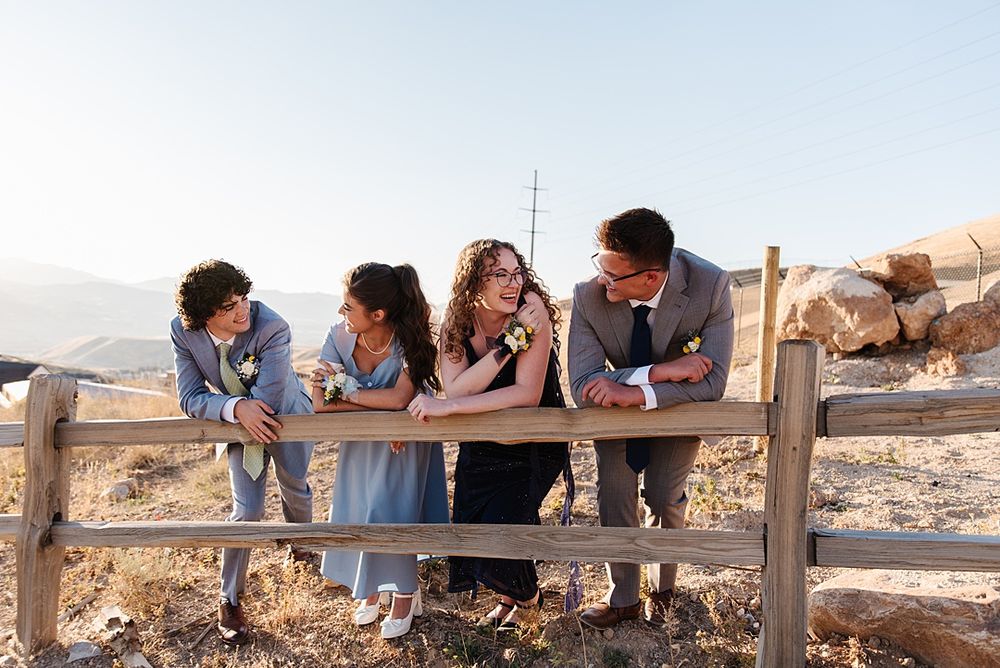 Group of people leaning on wooden fence while laughing together outdoors.