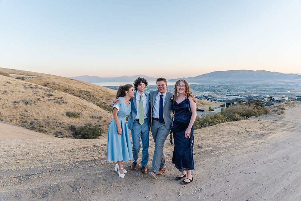 Group posing together on dirt path with scenic mountain valley view in background.