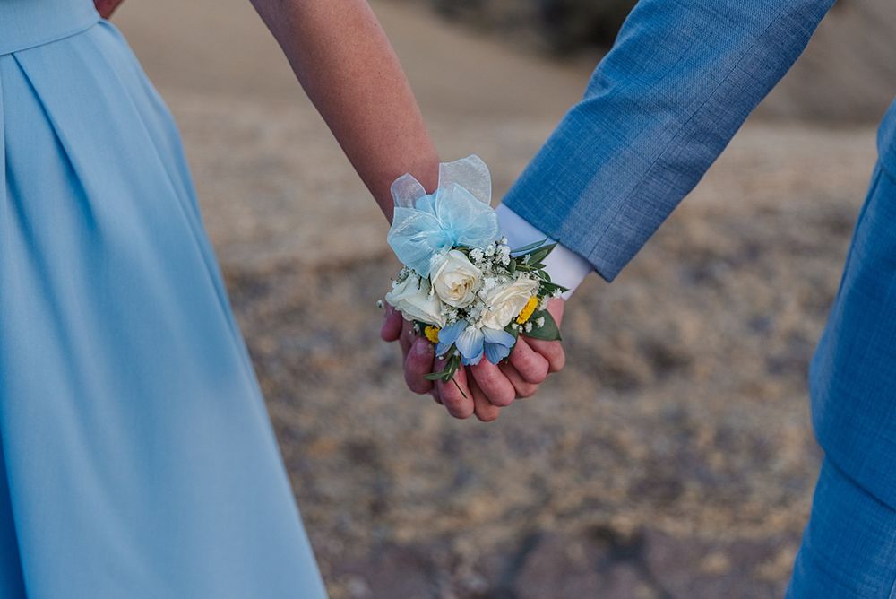 Two hands holding delicate white and blue flower corsage against blurry background.