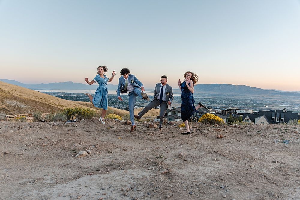 Group jumping in sync on mountain ridge during sunset with scenic valley backdrop.