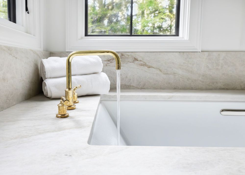 Luxurious bathroom sink with gold faucet and marble countertop next to folded white towels.