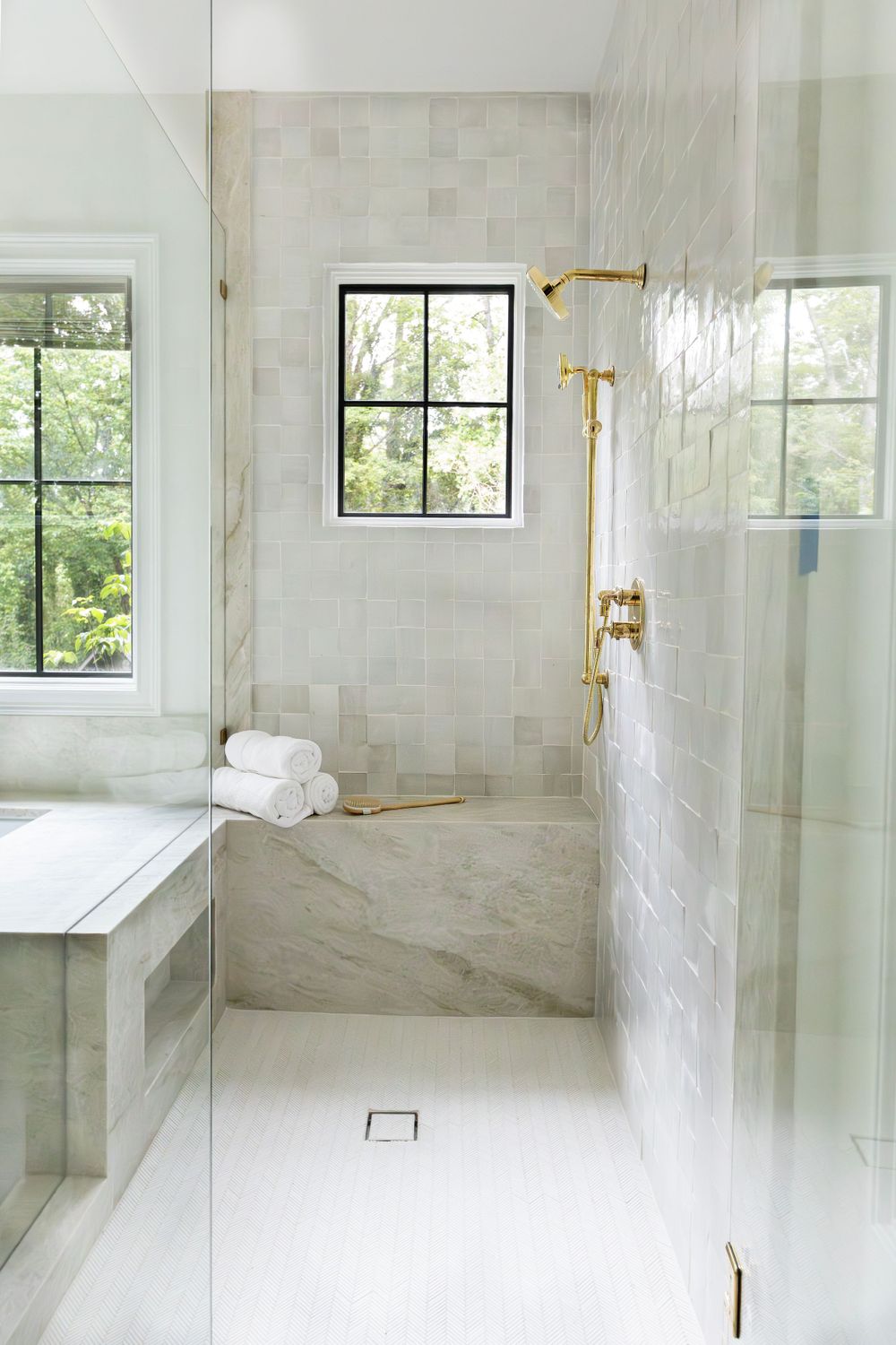 Luxurious marble bathroom with glass shower, brass fixtures and large windows.