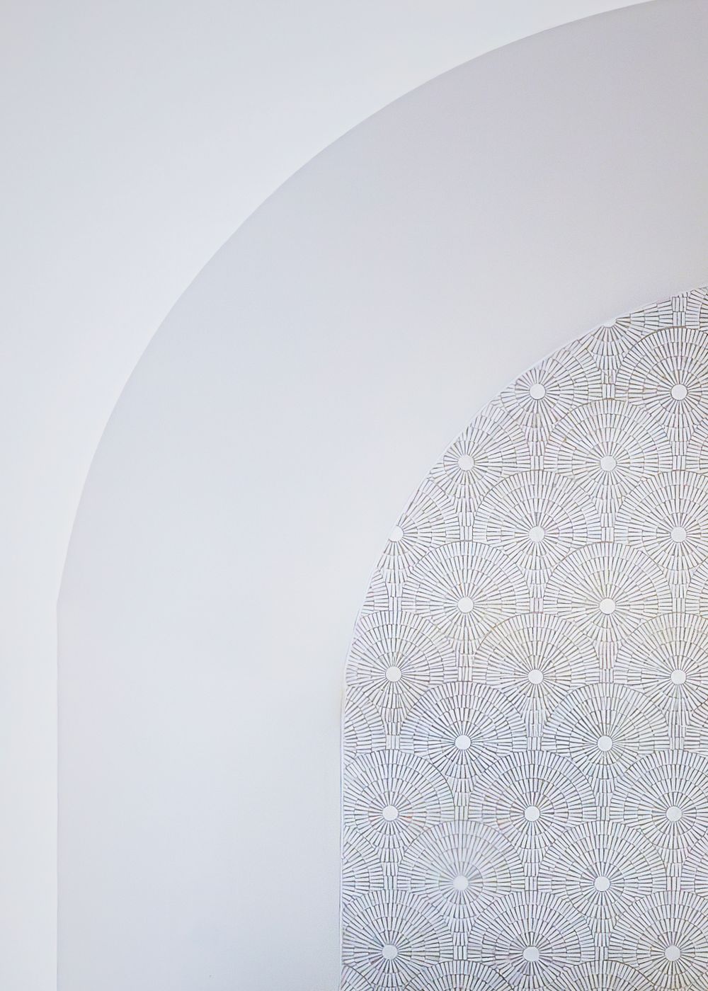 Minimalist white wall with delicate scalloped pattern detail in an arched alcove.