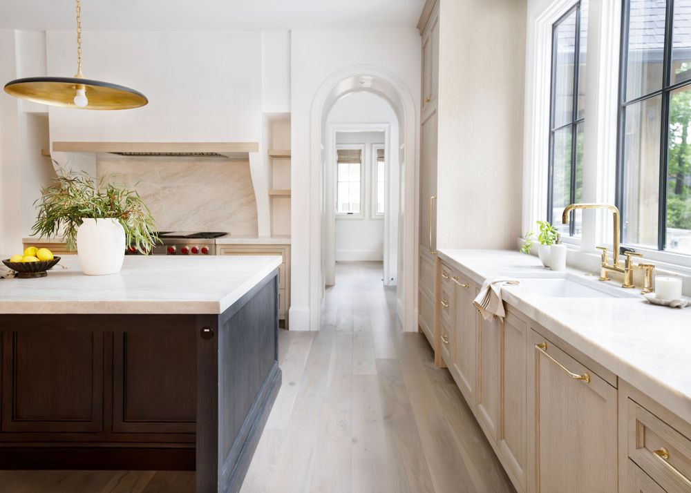 Long galley kitchen with navy island, wood cabinets and brass pendant lights.