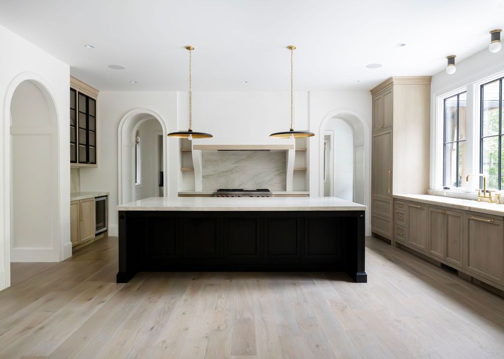 Spacious kitchen featuring arched doorways, black center island and light wood flooring.