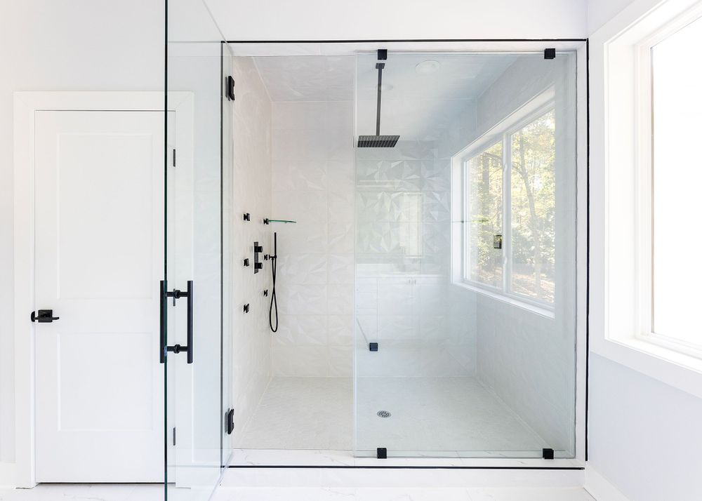 Minimalist glass shower enclosure with black hardware and large window for natural light.