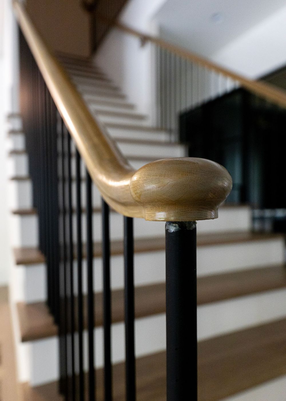 Close-up detail of wooden handrail and black metal balusters on a modern staircase.