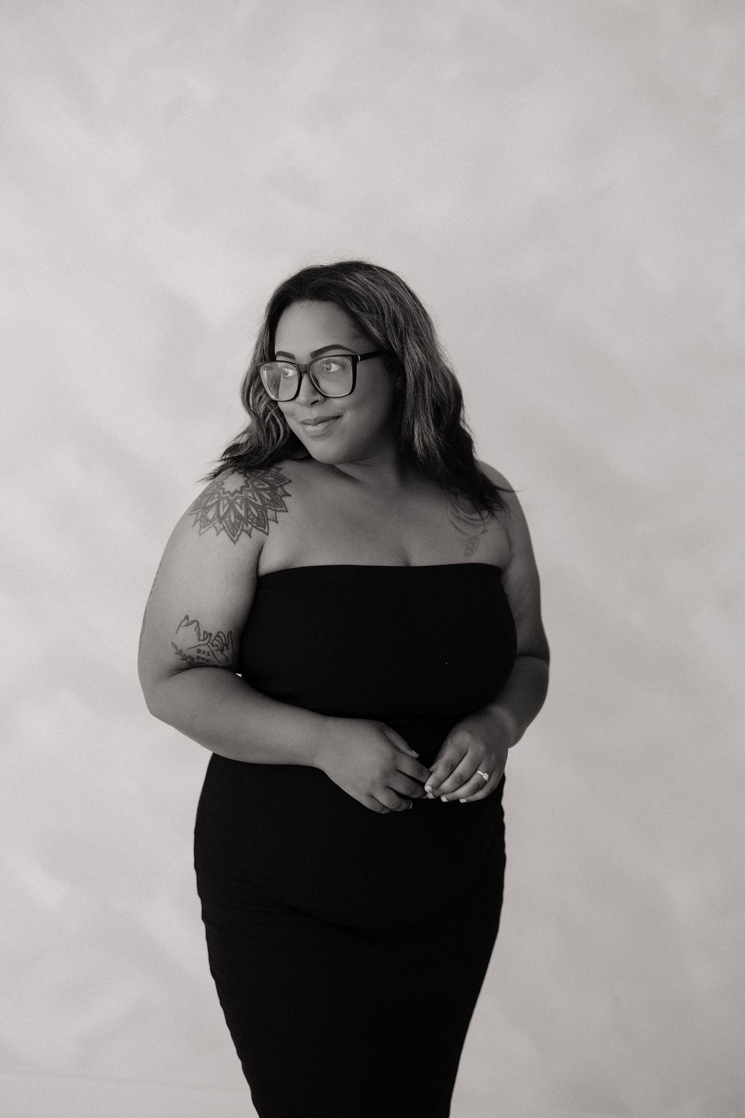 Woman in black midi dress poses against white draped backdrop with pampas grass decor.