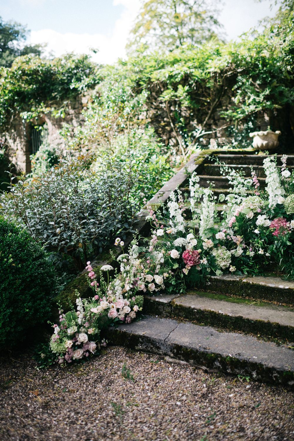 Beautiful garden path lined with blooming white and pink roses climbing over rustic wooden structures.