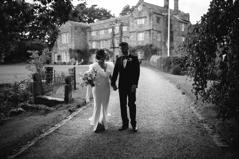 A romantic black and white photo series of a couple walking down a tree-lined path in formal attire.