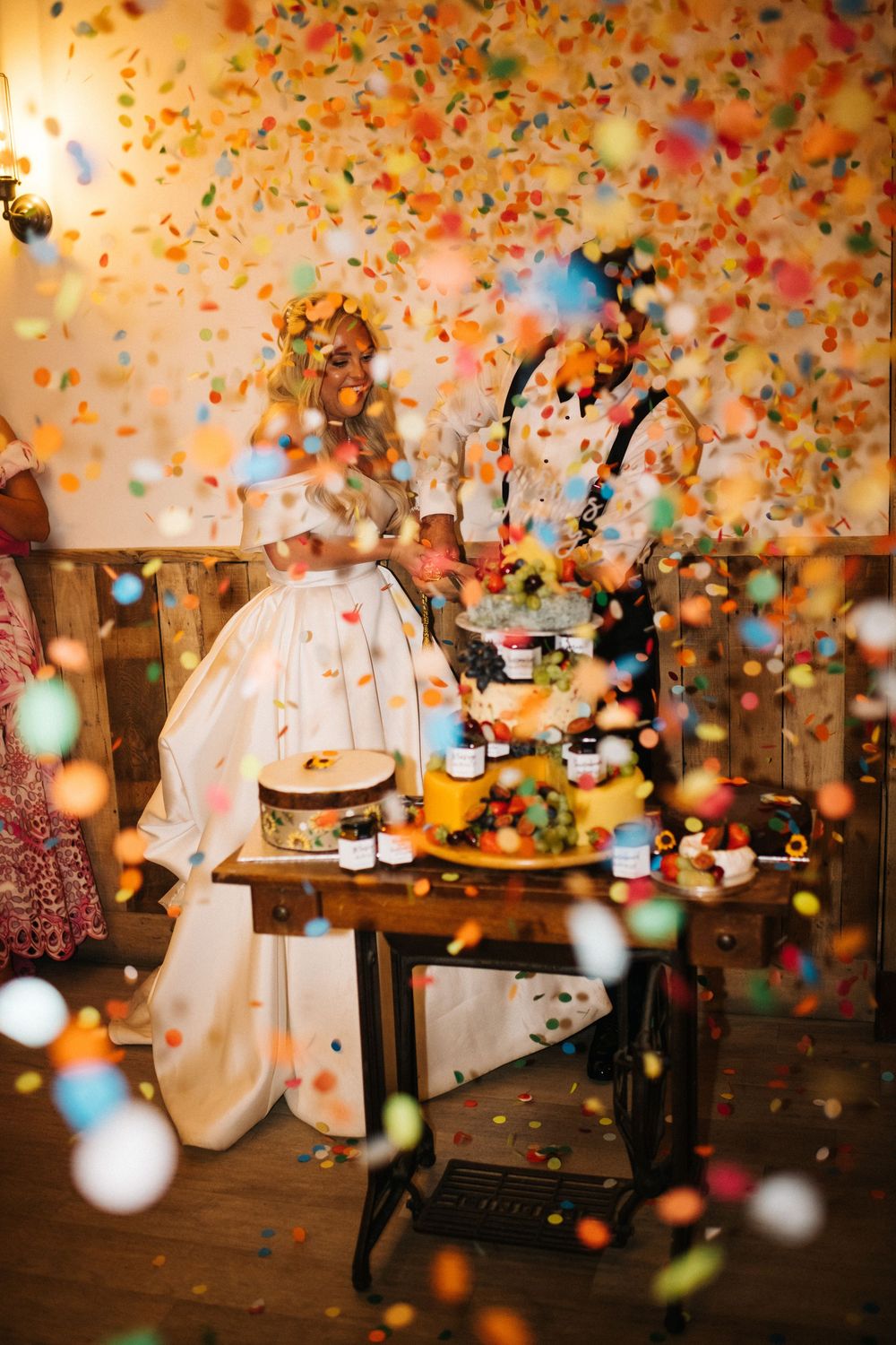 Colorful confetti and balloons fill the air during a joyful celebration in a dimly lit room with festive decorations.