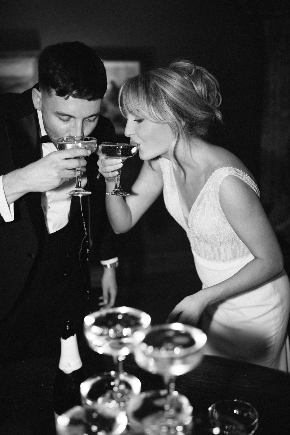 Black and white photo of wedding party toasting with champagne glasses in intimate setting.
