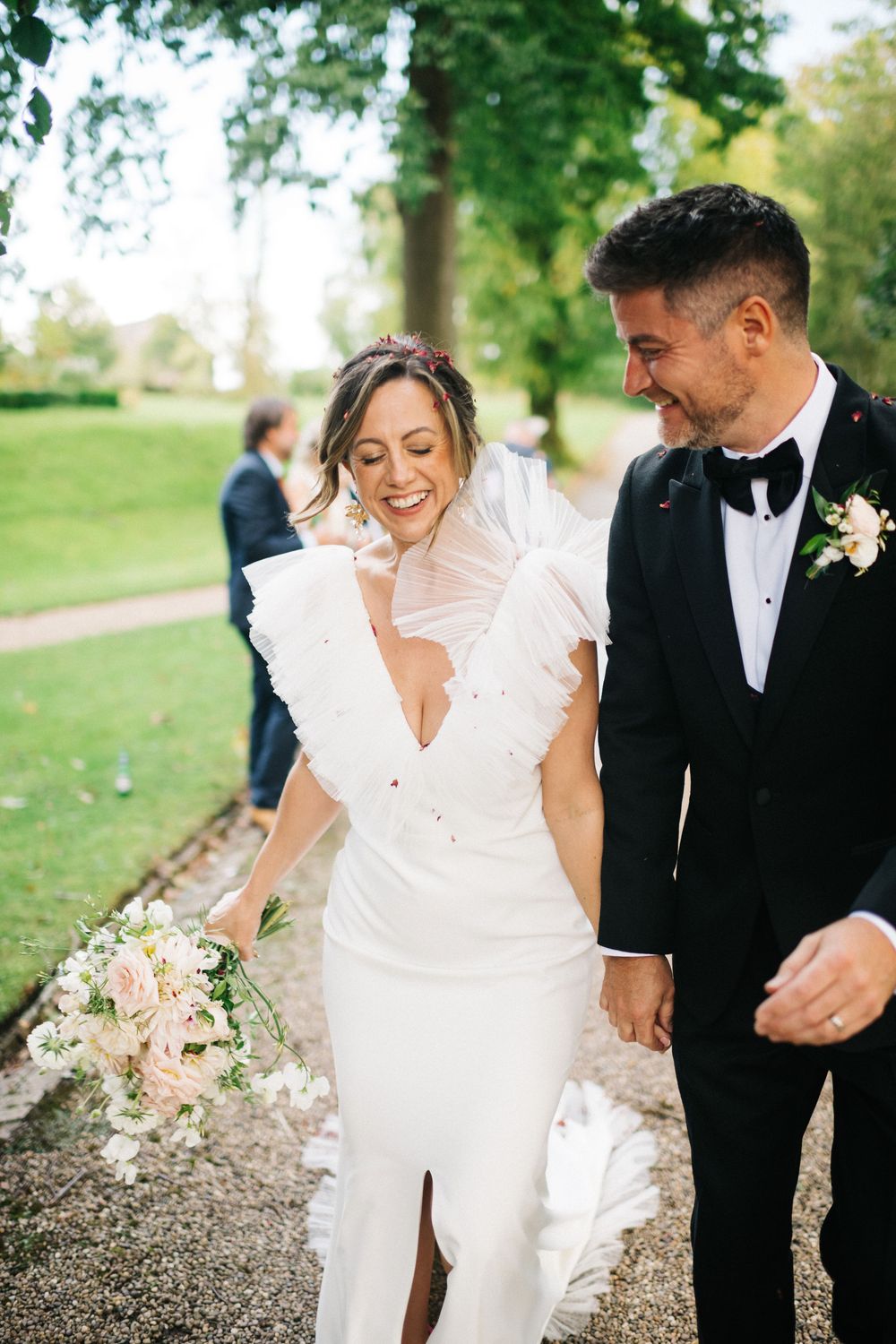 A wedding couple shares a joyful moment walking outdoors with the bride in a modern white dress.