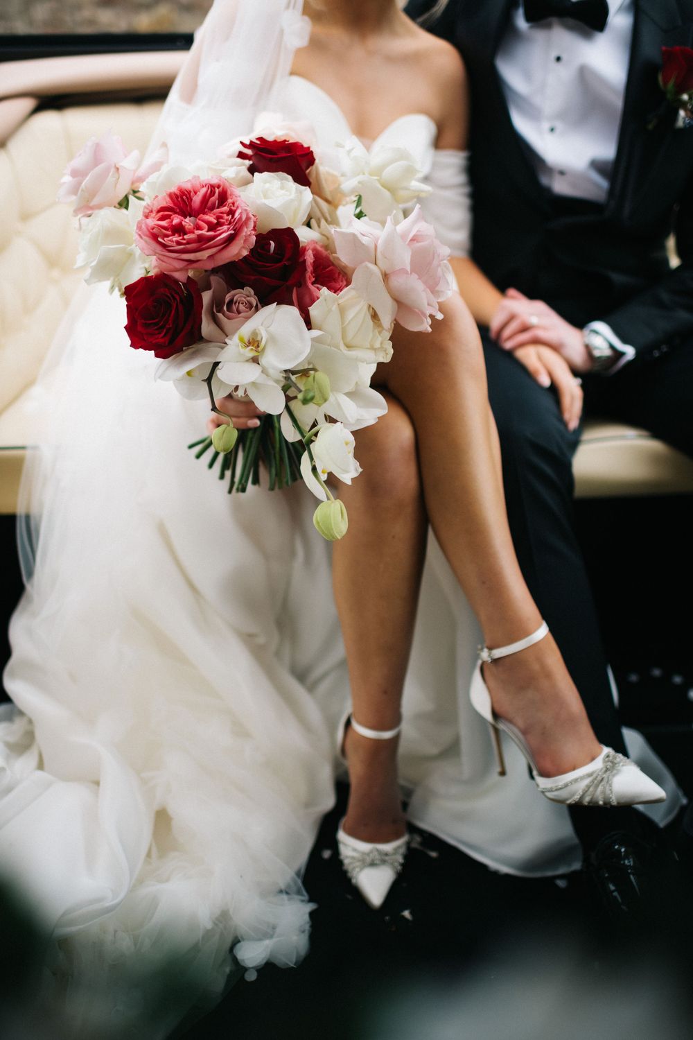 Close-up details of wedding bouquets featuring red roses and white flowers against formal attire.