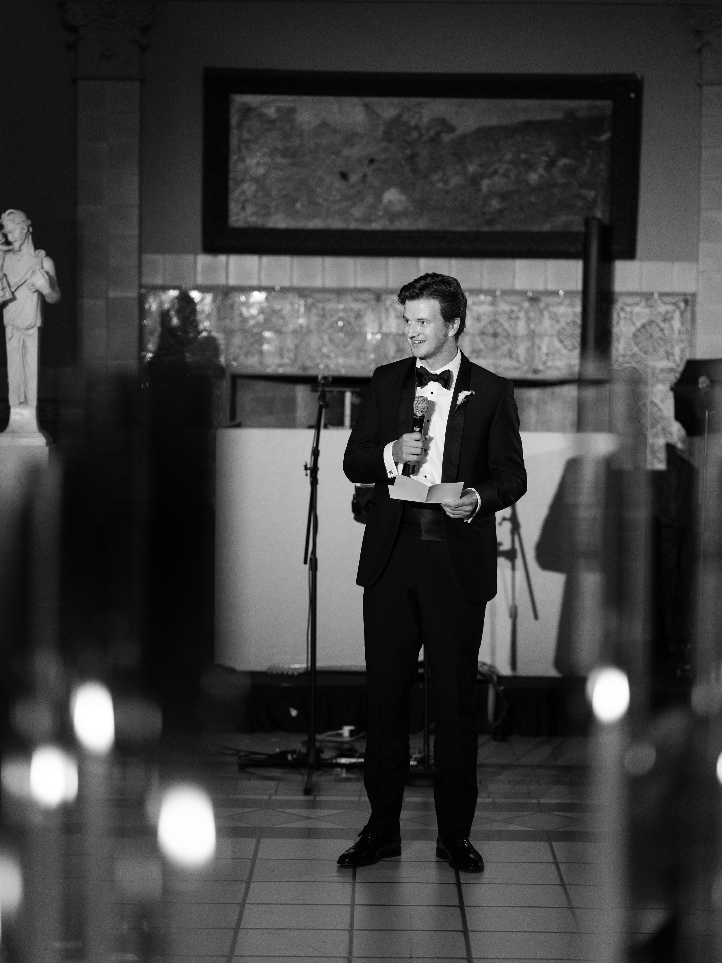 Black and white photo of formal event with dramatic lighting and microphone stands.