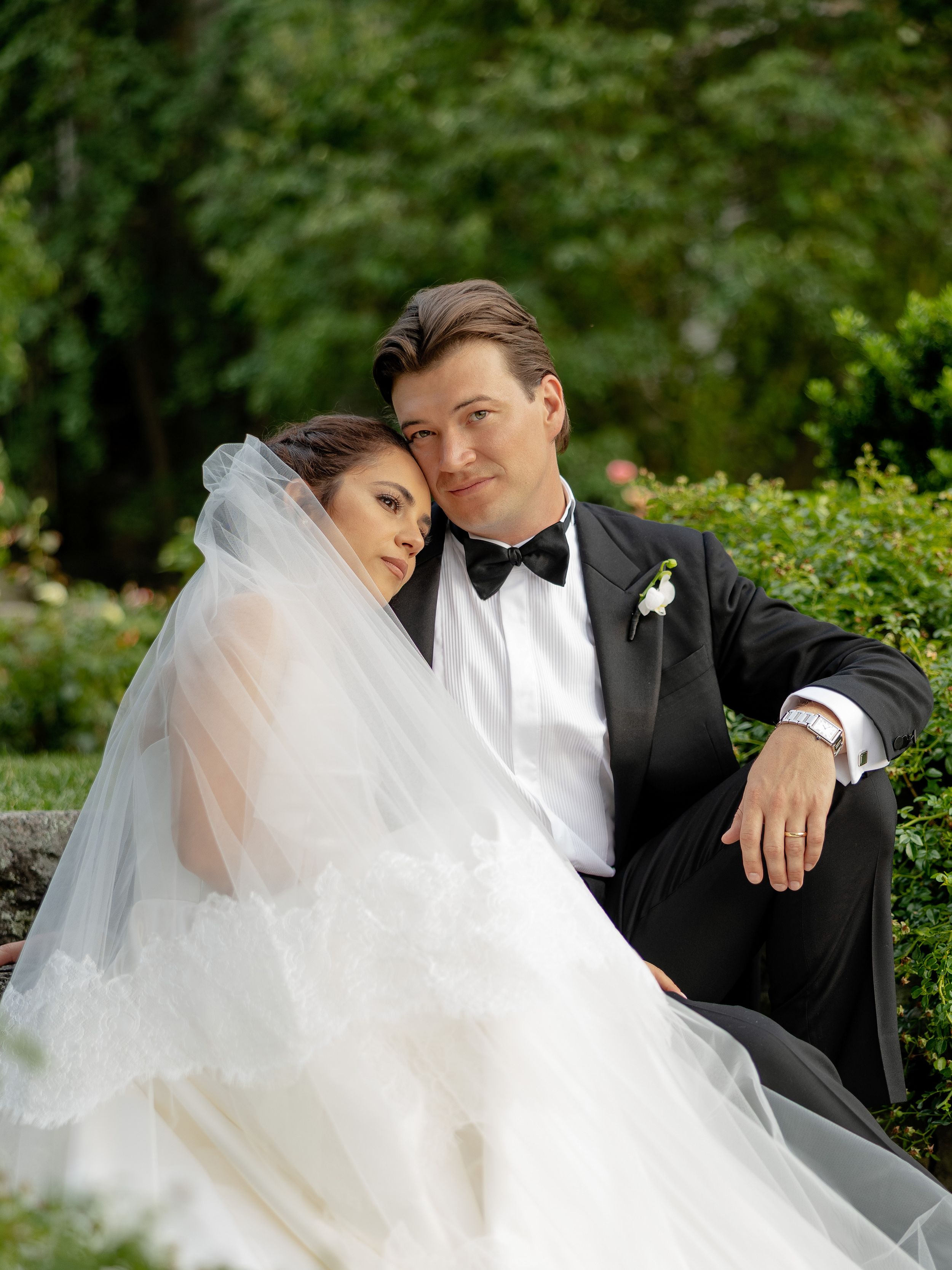 A romantic wedding couple poses together on lush garden grounds.