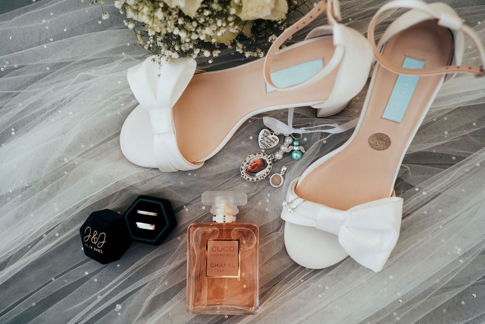 Elegant white wedding shoes and perfume bottles arranged on a gray wooden floor with baby's breath flowers.