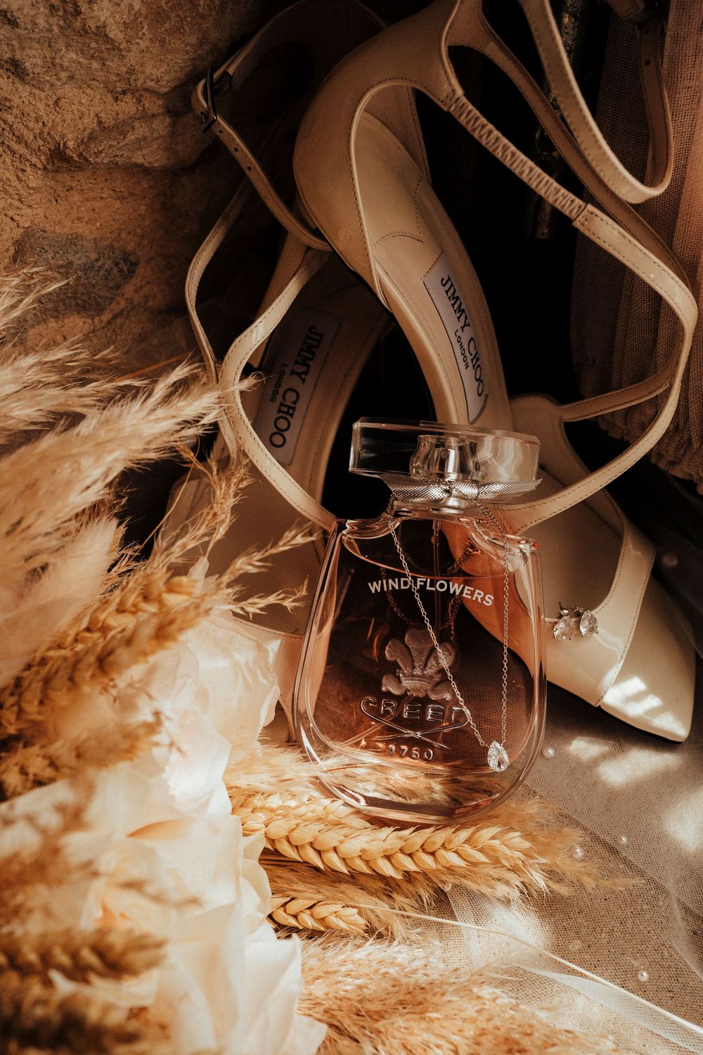 Elegant high heel shoes and perfume bottle styled with dried wheat stems in warm sepia tones.