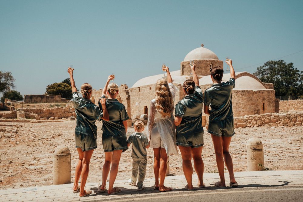 A group of tourists pose with raised arms in front of ancient stone ruins in a desert landscape.