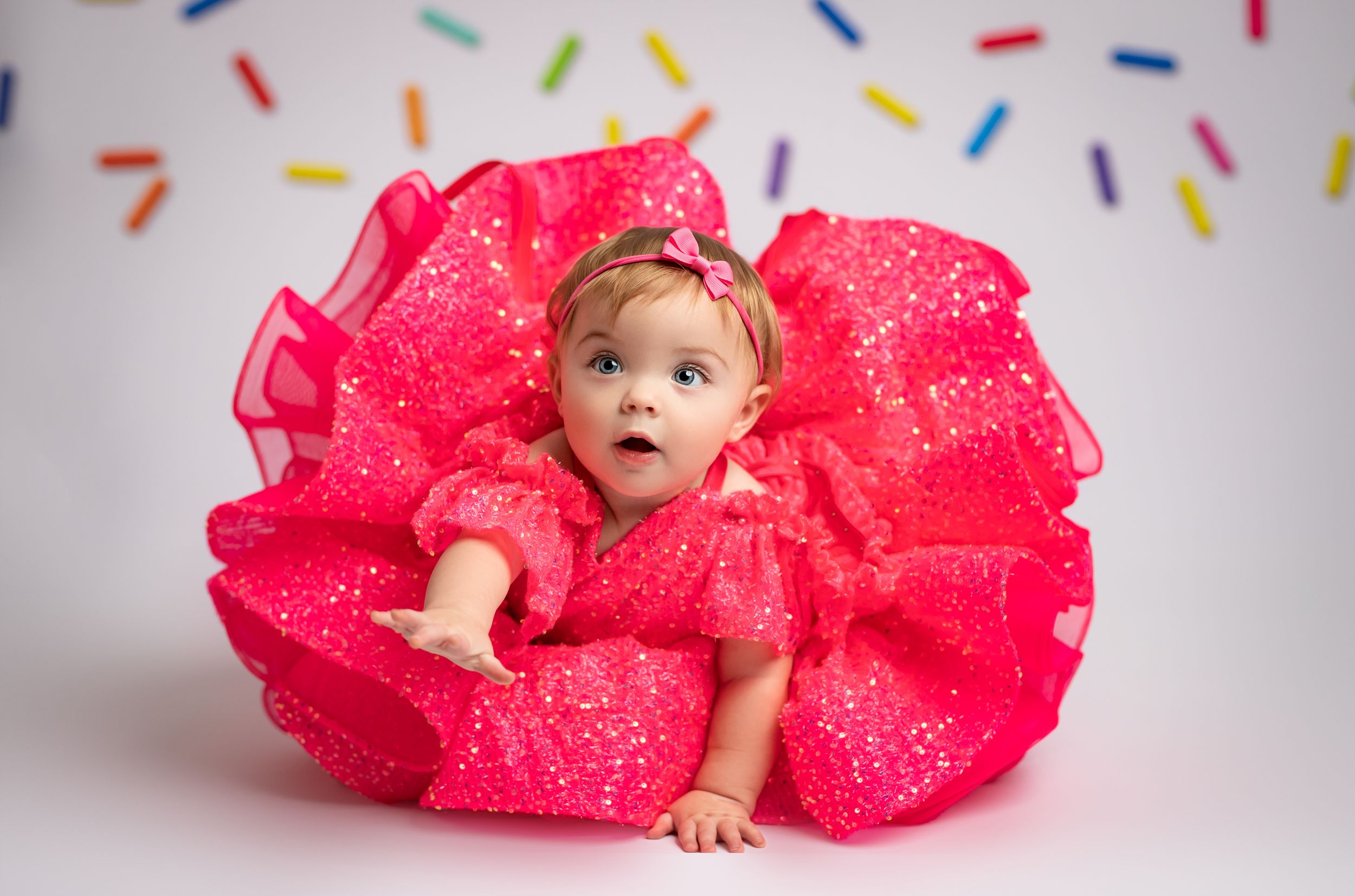 Baby wearing bright pink tulle dress poses on white backdrop in multiple artistic shots.