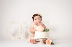 Soft pink and white cake smash photography setup with floral decorations and delicate lighting.