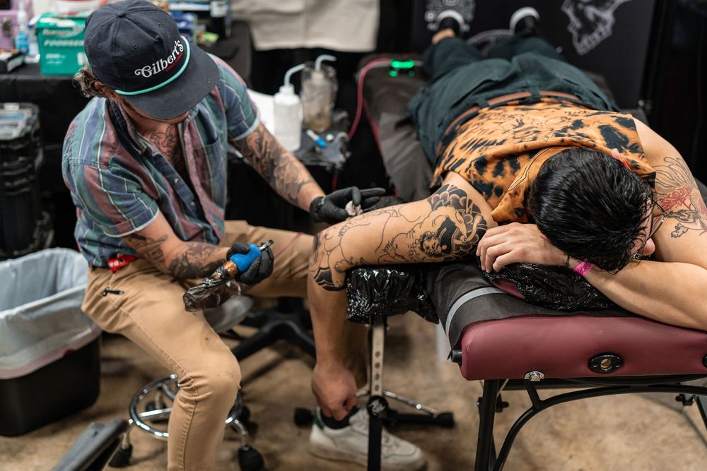 Tattoo artist inking detailed back piece on client at tattoo convention.
