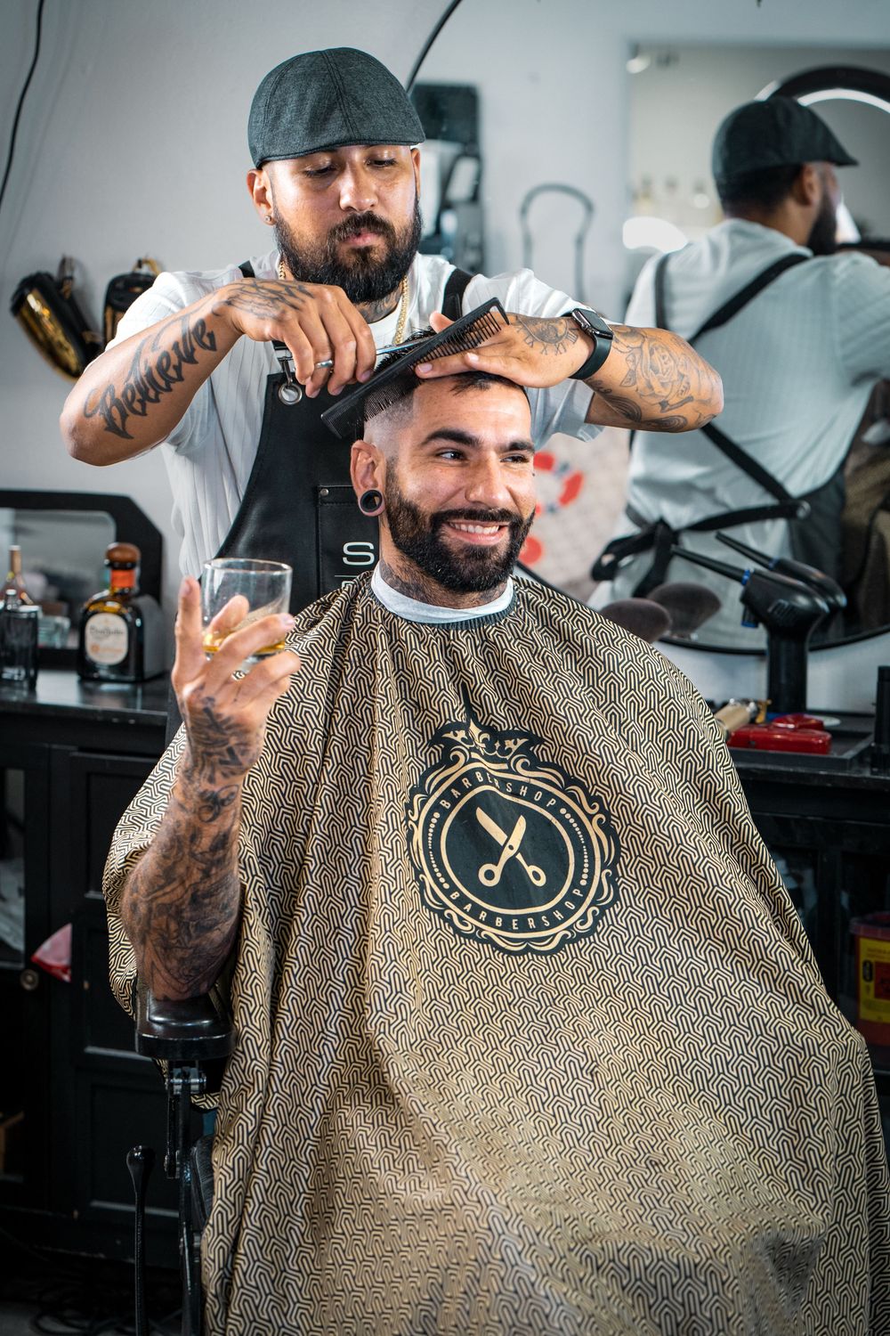 Smiling client giving thumbs up while barber styles hair in bright barbershop.