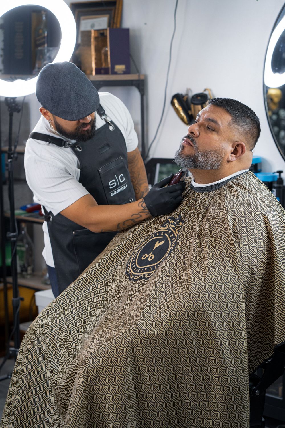 Barber trimming beard of client draped in ornate cape at professional barbershop.