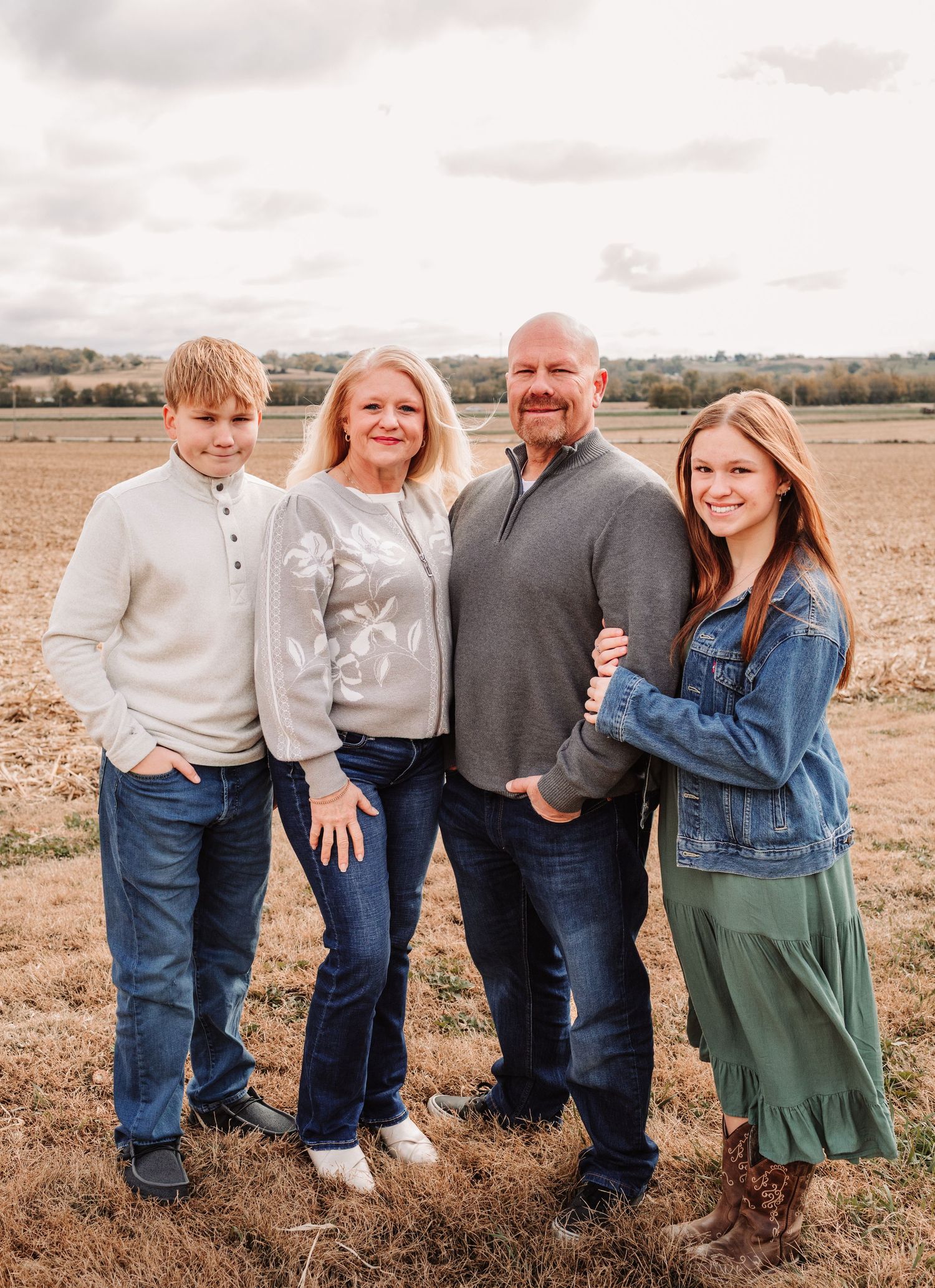 Family of four in coordinated outfits posing in a harvested autumn field under cloudy skies.