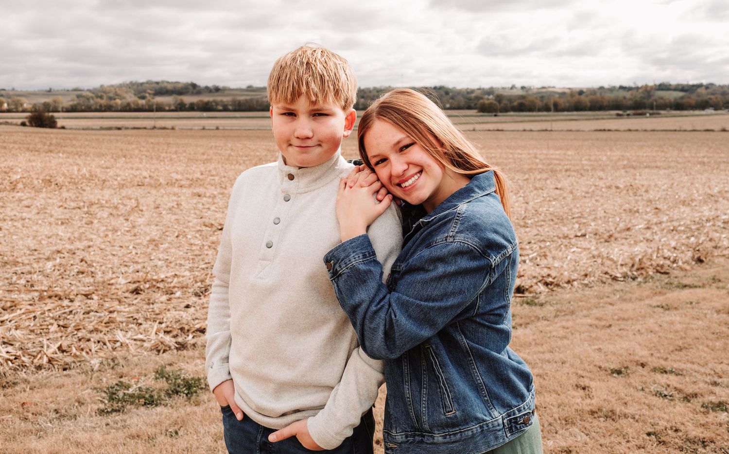 Two siblings, a boy and teenage girl, posing together affectionately in a fall harvest field.