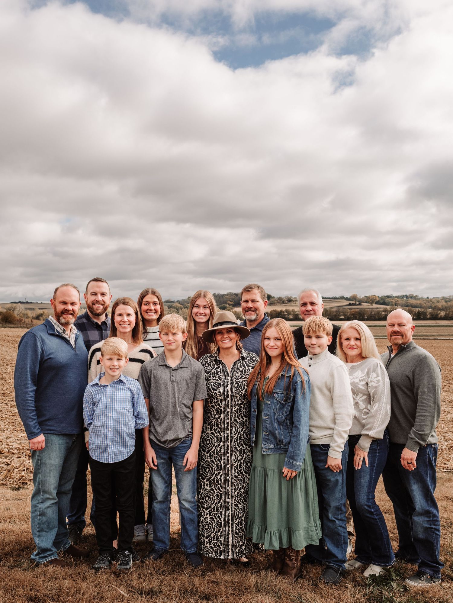 Large extended family group portrait outdoors in a wide open field under dramatic cloudy skies.