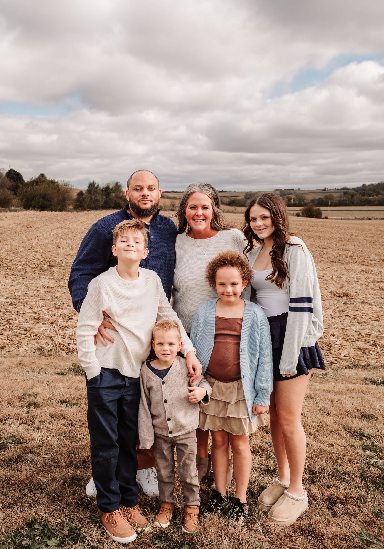Family of six posing together in an open farm field, including parents and four children of varying ages.