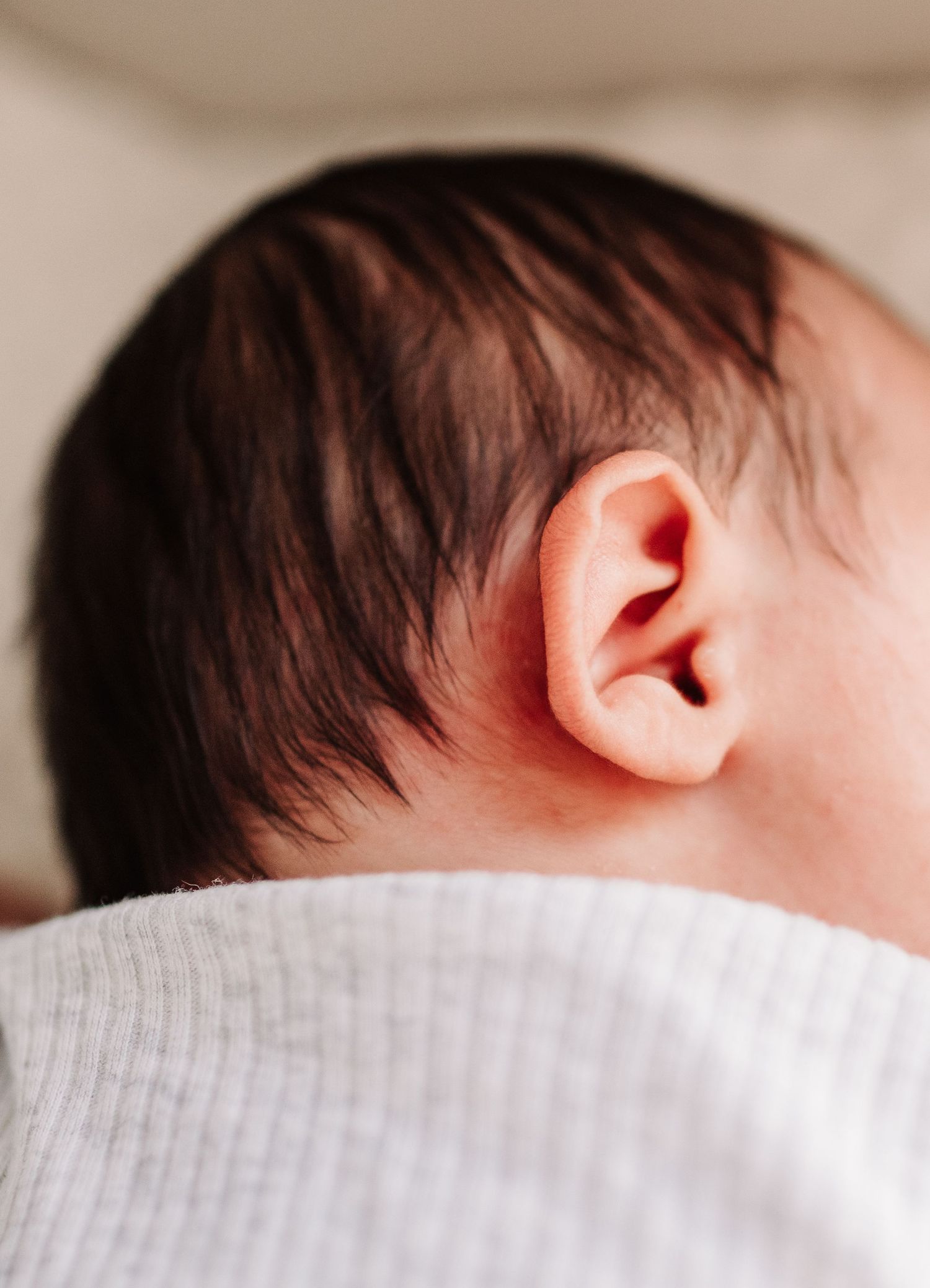 Close-up of a newborn baby's ear and dark hair, resting peacefully against a white fabric.