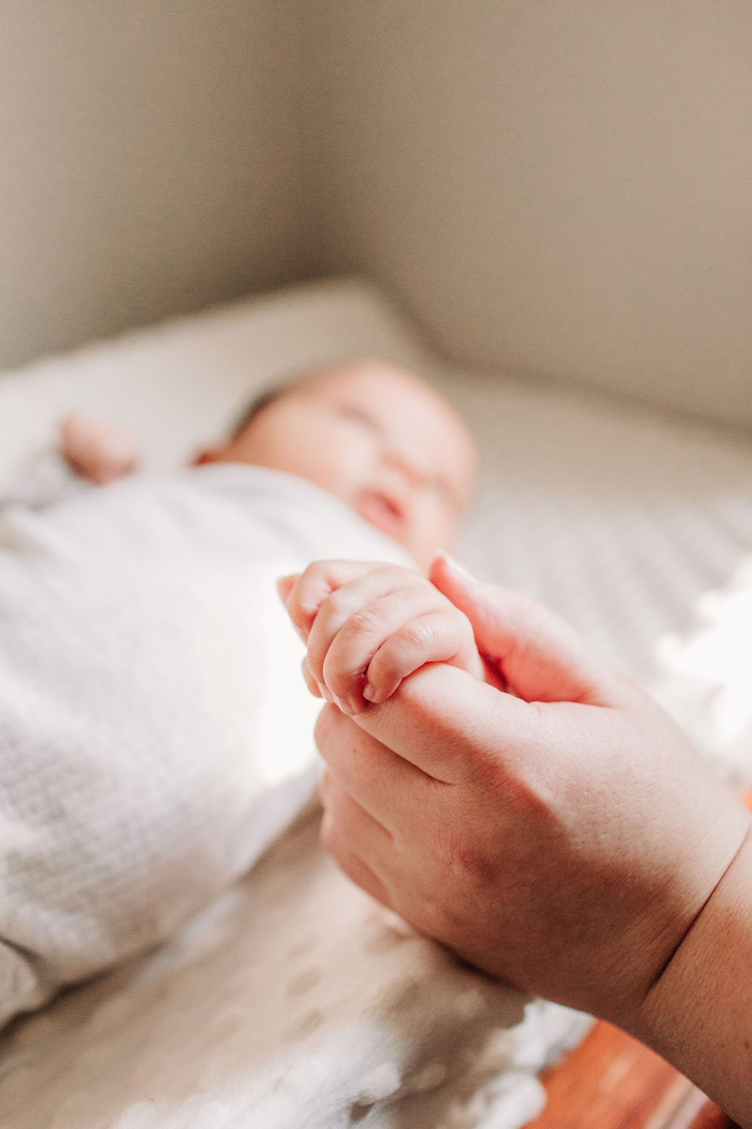 Close-up of a newborn baby grasping an adult finger while lying on a white blanket.