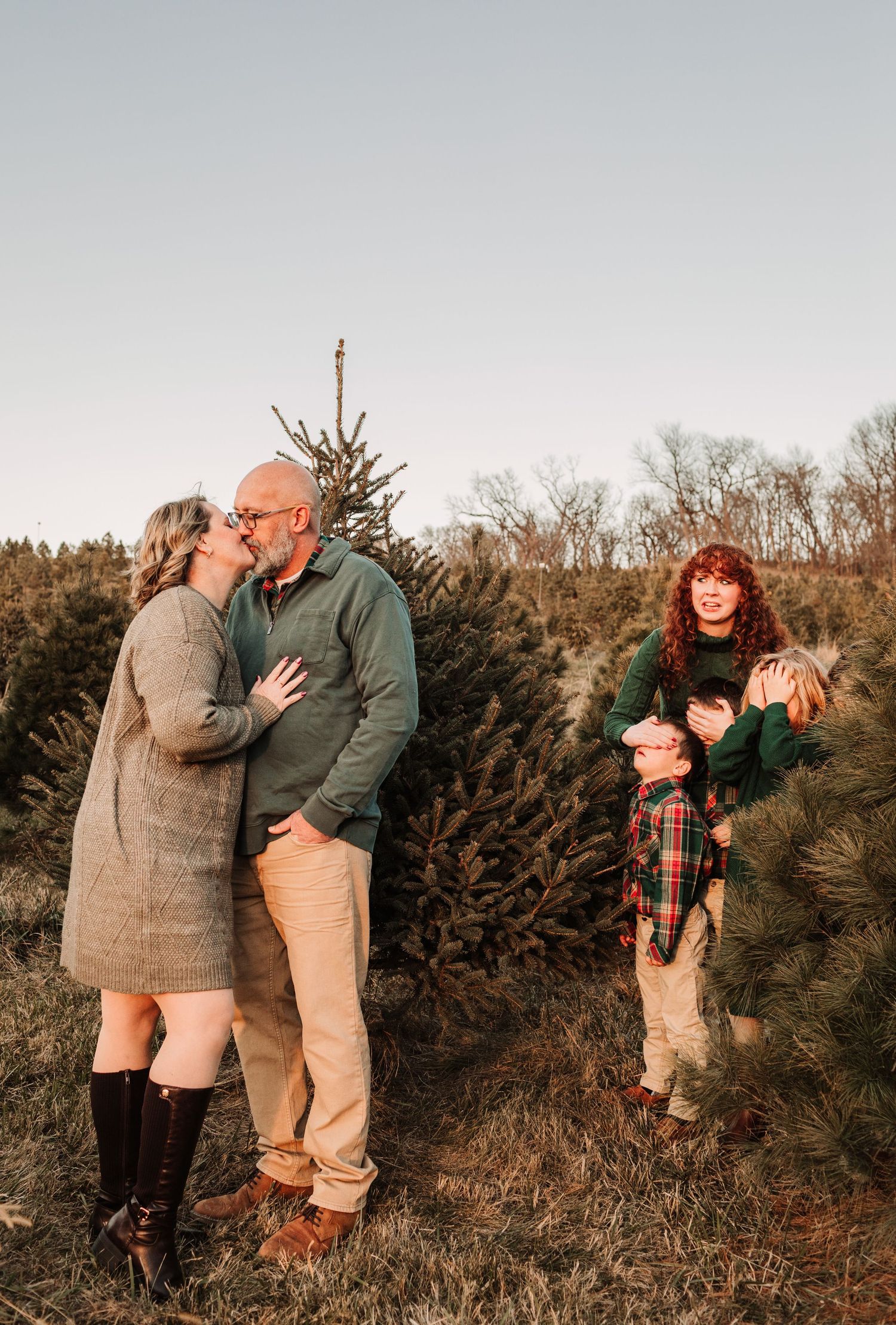 Family sharing a joyful moment together among Christmas trees at an outdoor tree farm.