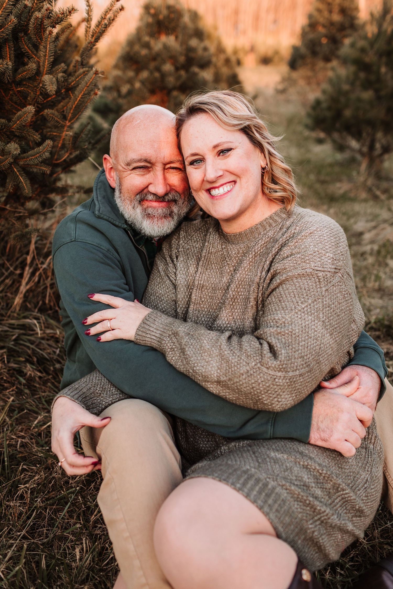 Happy couple embracing and smiling together while sitting among evergreen trees outdoors.