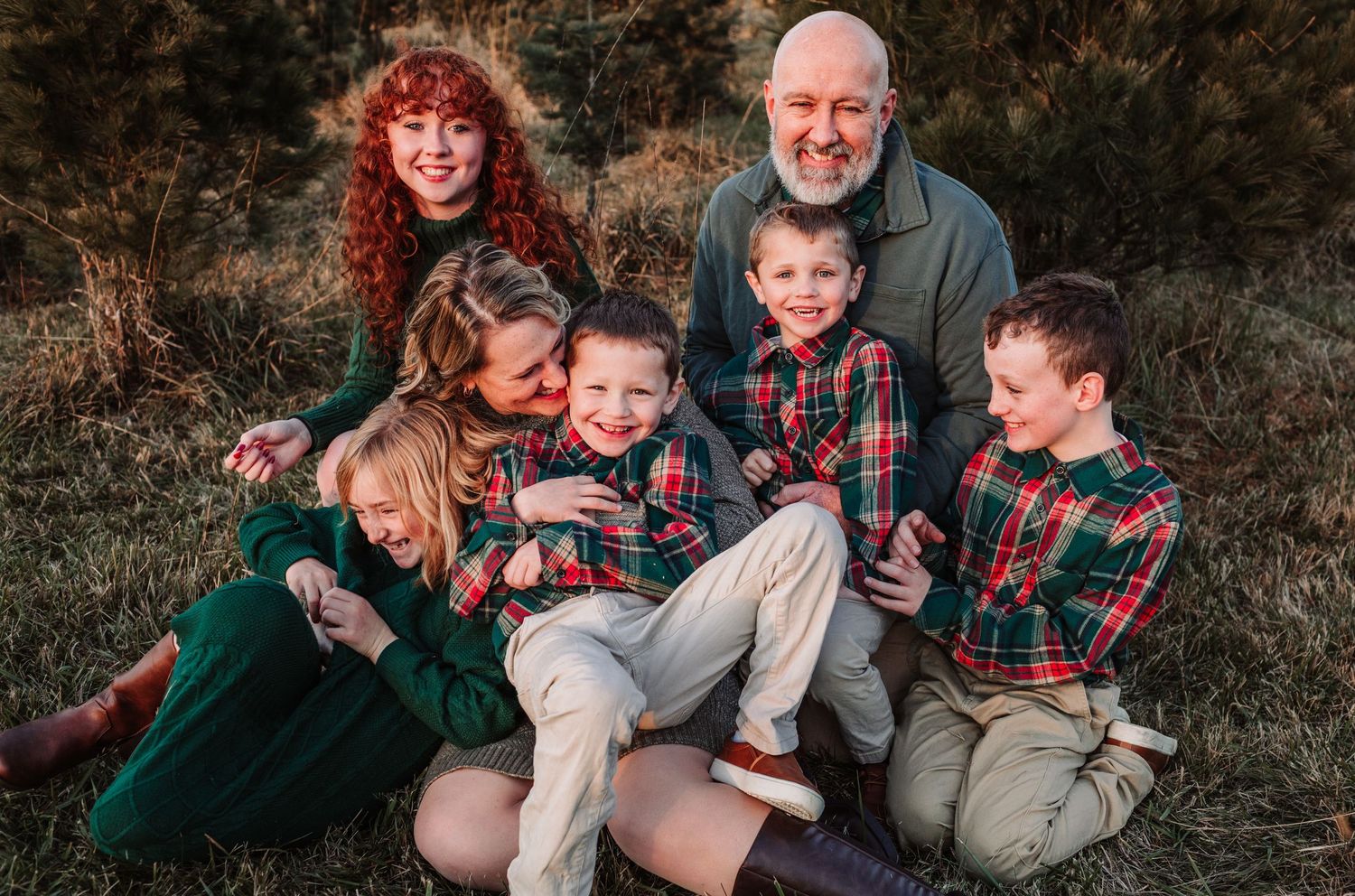 Large family of seven smiling together outdoors in festive green and plaid holiday outfits during a Christmas photo session.